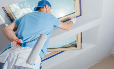 Caucasian Worker Putting Finishing Touches on Corners Around the Window Painting Them with White Paint Using Small Paint Brush. Preparation of Apartments in New Residential Building.